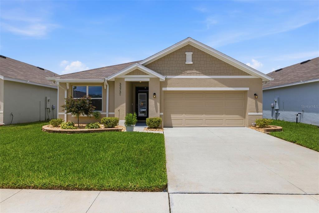 A single-story suburban house with a tan stucco exterior, a two-car garage, and a lawn — 33731 HAMILTON HILL LANE, WESLEY CHAPEL, FL