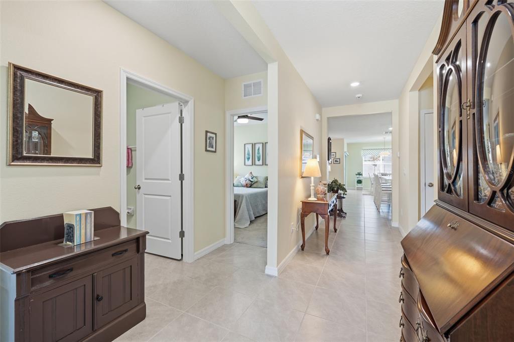 A tiled hallway leads past a bedroom and console table toward a bright dining area — 33731 HAMILTON HILL LANE, WESLEY CHAPEL, FL