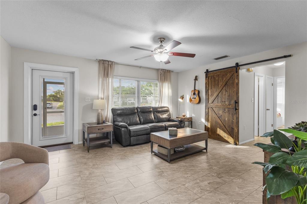A living room features tile flooring, a leather sofa, a ceiling fan, and a barn door — 3015 SOUTHERN PARKWAY W, BRADENTON, FL