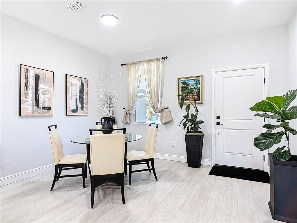 A dining area features a glass table, four chairs, light wood flooring, and a white door — 1785 9TH AVENUE, DELAND, FL