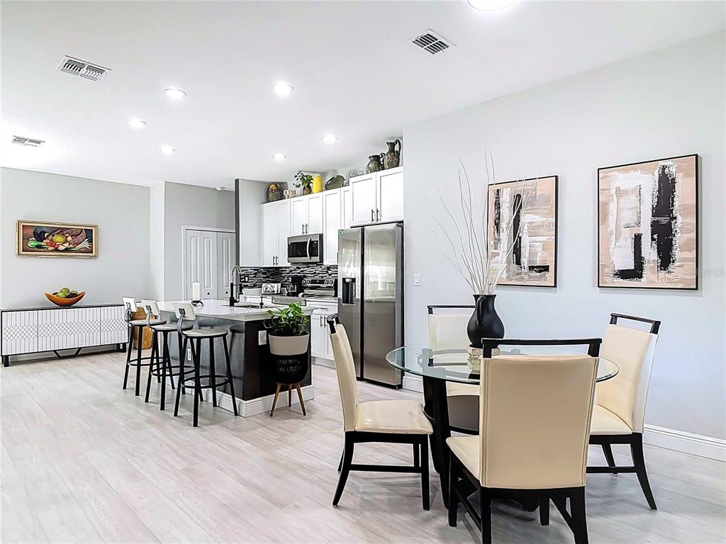 A kitchen with white cabinets and a dining area with a glass table and chairs — 1785 9TH AVENUE, DELAND, FL
