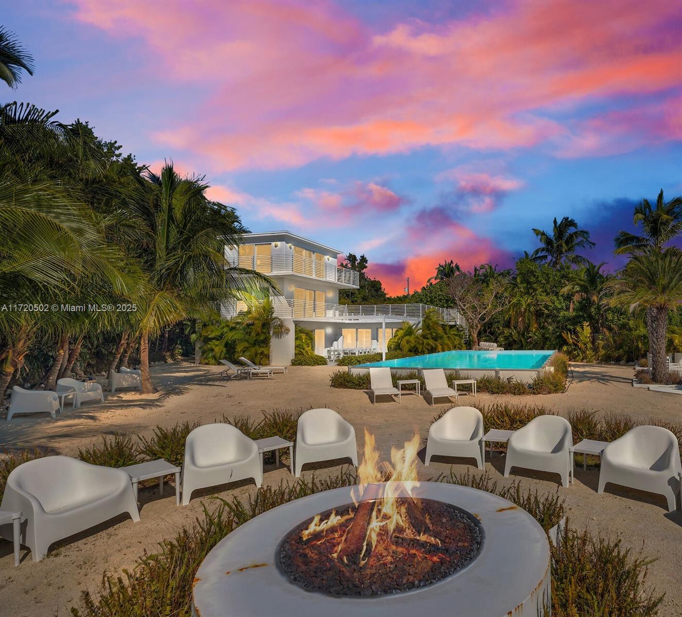 A fire pit with white chairs sits on a sandy patio before a modern house — 98701 Overseas Hwy, Key Largo FL 33037, KEY LARGO, FL