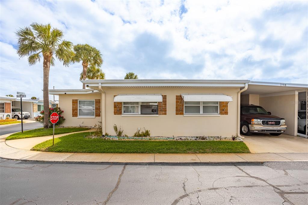 A single-story beige house with a carport, two windows with awnings, and a palm tree — 250 ROSERY ROAD NW UNIT 298, LARGO, FL