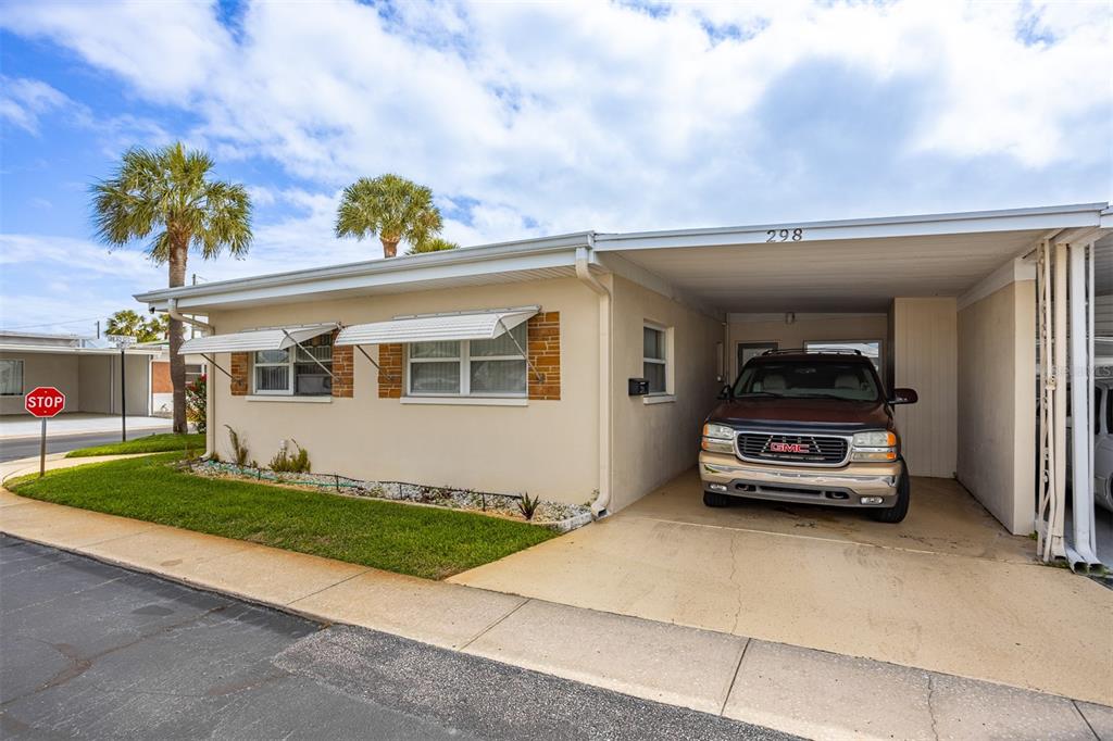 A single-story house with a beige exterior, a carport, and a GMC SUV parked inside — 250 ROSERY ROAD NW UNIT 298, LARGO, FL