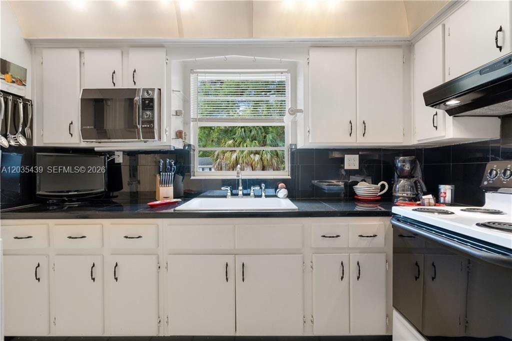 A kitchen features white cabinets, black countertops, a black tile backsplash, and a window — 2916 12th Ave, Vero Beach FL 32960, VERO BEACH, FL