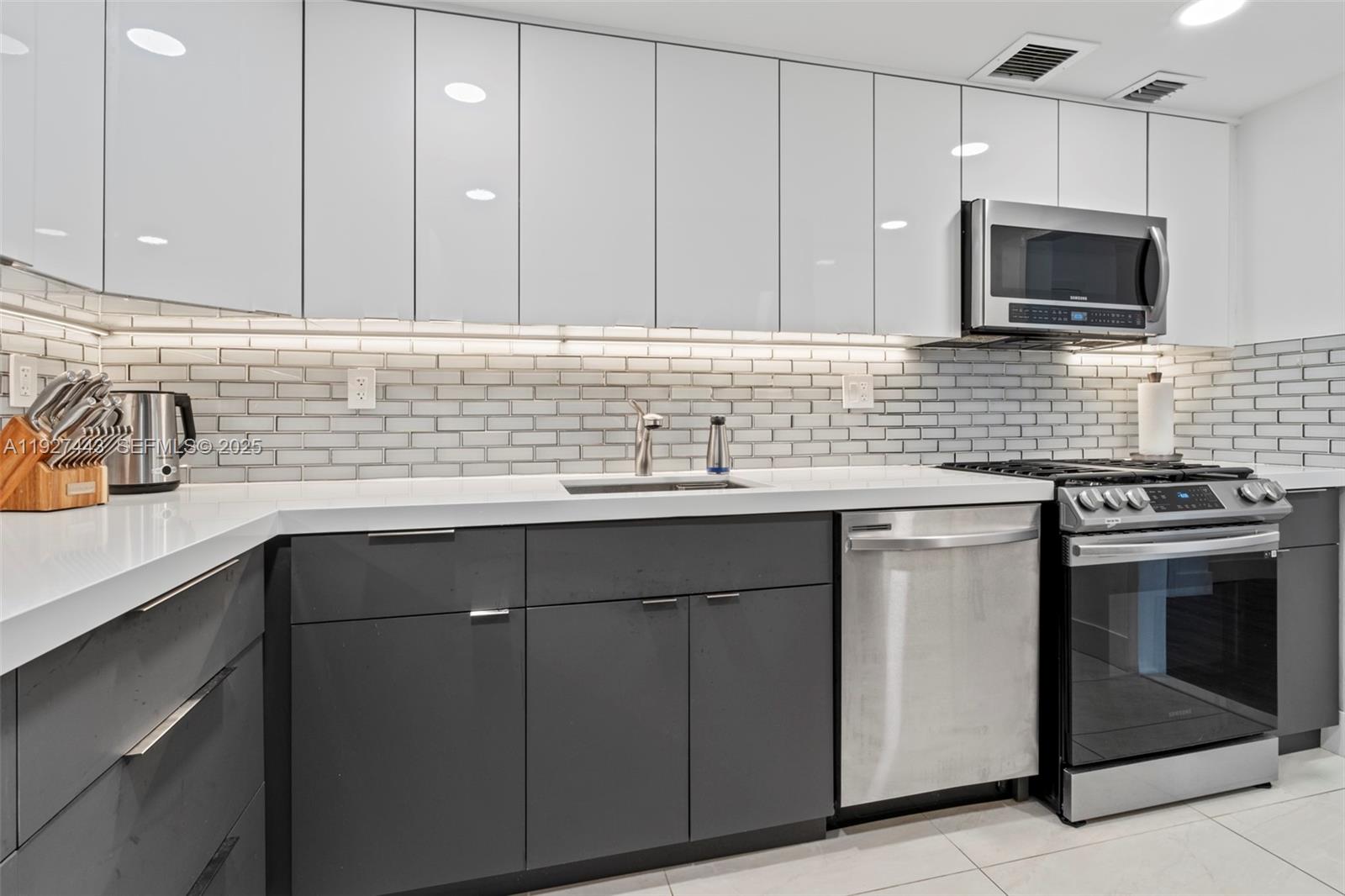 A modern kitchen features white upper cabinets, dark grey lower cabinets, and a subway tile backsplash — 3140 S Ocean Dr # 511, Hallandale Beach FL 33009, HALLANDALE BEACH, FL