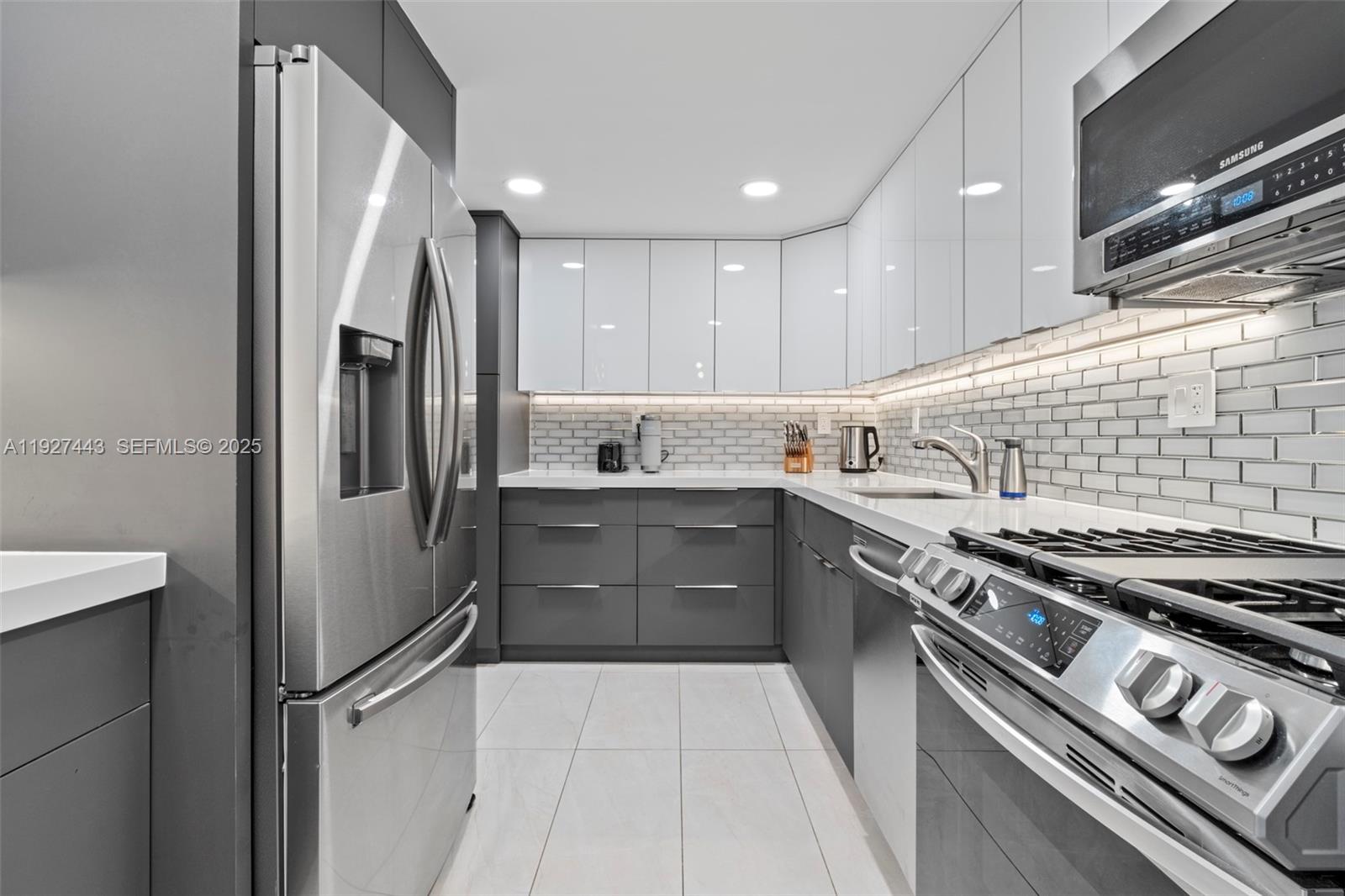 A modern kitchen features gray lower cabinets, white upper cabinets, stainless steel appliances, and tile — 3140 S Ocean Dr # 511, Hallandale Beach FL 33009, HALLANDALE BEACH, FL