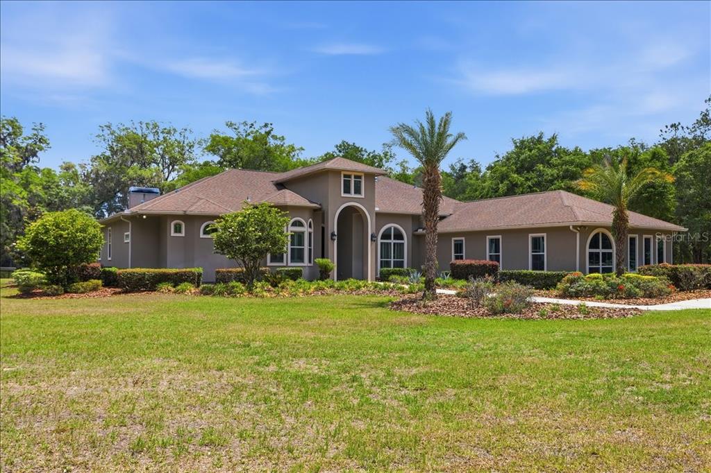 A single-story tan house with a brown roof and arched windows sits on a lawn — 7369 NW 187TH TERRACE, ALACHUA, FL