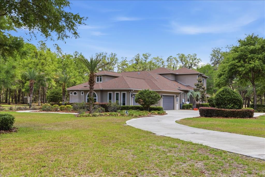 A large, two-story tan house with a multi-gabled roof and a concrete driveway — 7369 NW 187TH TERRACE, ALACHUA, FL