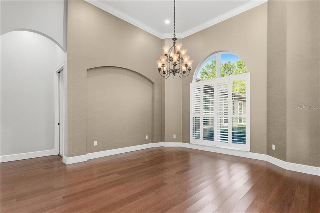 An empty dining room features high ceilings, a chandelier, arched wall niche, and hardwood floors — 7369 NW 187TH TERRACE, ALACHUA, FL