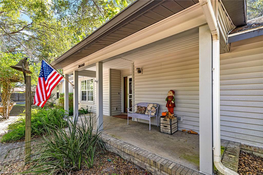 A covered front porch features a light-colored siding, a metal bench, and an American flag — 3644 SE 22ND AVENUE, OCALA, FL