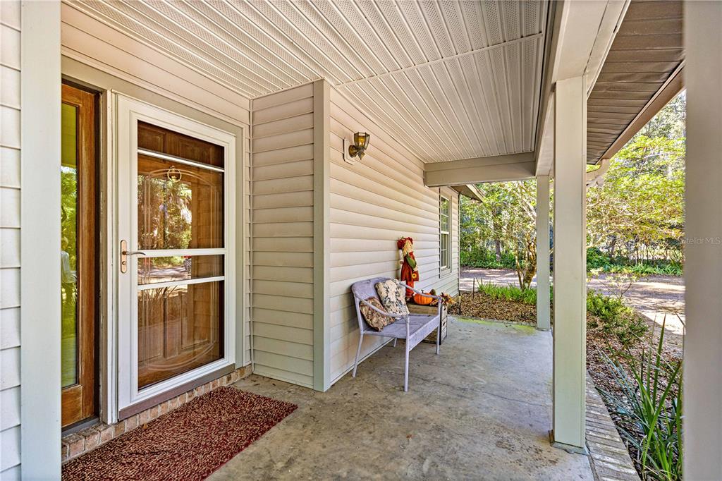 A covered porch features a light-colored bench, a storm door, and beige vinyl siding — 3644 SE 22ND AVENUE, OCALA, FL
