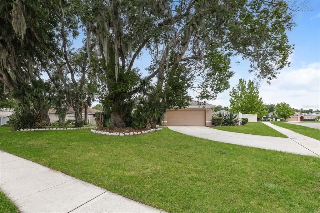 A single-story house with a two-car garage sits behind a large tree-filled front lawn — 814 COADE STONE DRIVE, SEFFNER, FL