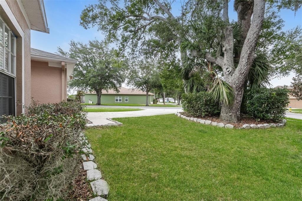 A grassy front yard features a large tree, stone garden borders, and a neighboring house — 814 COADE STONE DRIVE, SEFFNER, FL