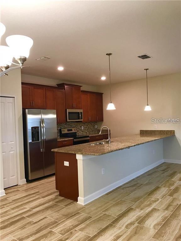 A kitchen features wood cabinets, stainless steel appliances, granite countertops, and a breakfast bar — 1599 MOON VALLEY DRIVE, DAVENPORT, FL