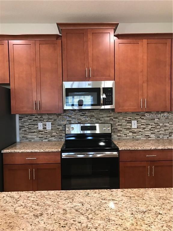 A kitchen features cherry-toned cabinets, granite countertops, a stainless steel microwave, and a tiled backsplash — 1599 MOON VALLEY DRIVE, DAVENPORT, FL