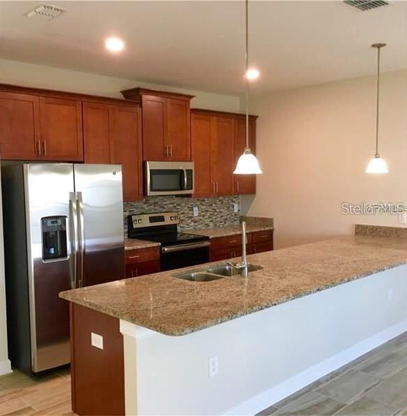 A kitchen features wood cabinets, stainless steel appliances, and a granite-topped island with pendant lighting — 1599 MOON VALLEY DRIVE, DAVENPORT, FL