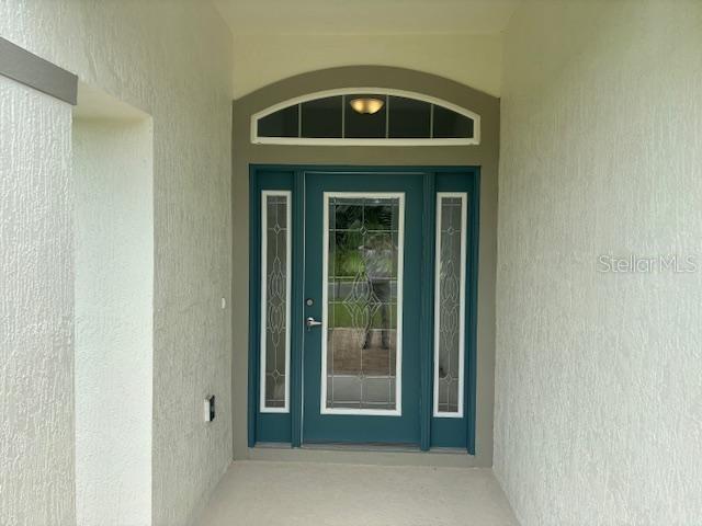 A teal front door with glass panels and an arched transom window sits in a stucco entryway — 7673 SW 180TH CIRCLE, DUNNELLON, FL