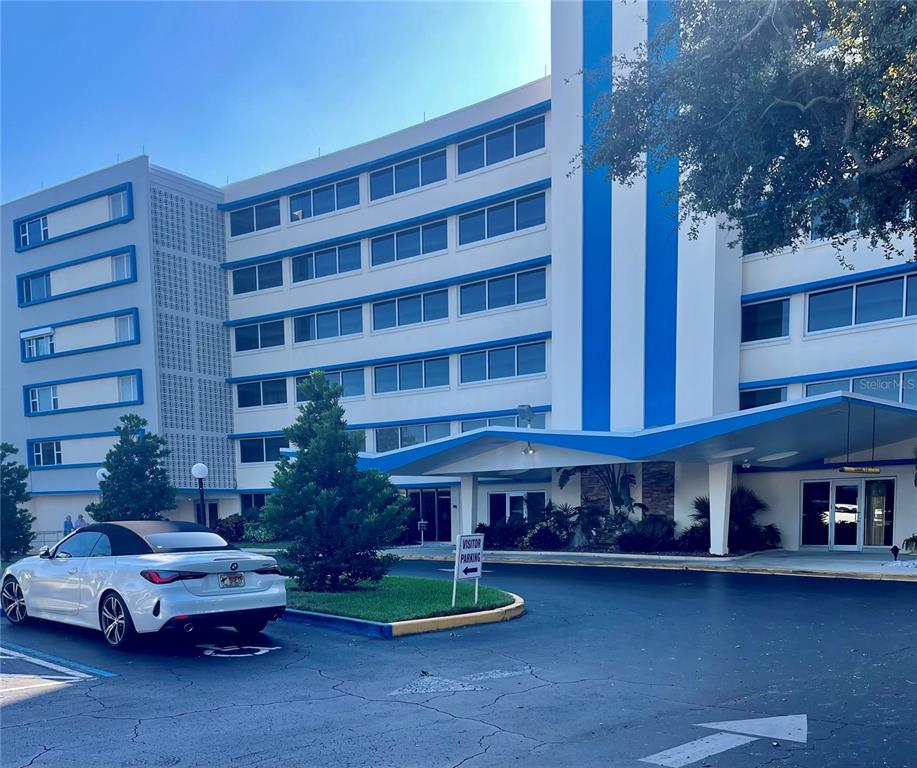 A white multi-story building with blue accents features a covered entrance and visitor parking — 1224 S PENINSULA DRIVE UNIT 304, DAYTONA BEACH, FL