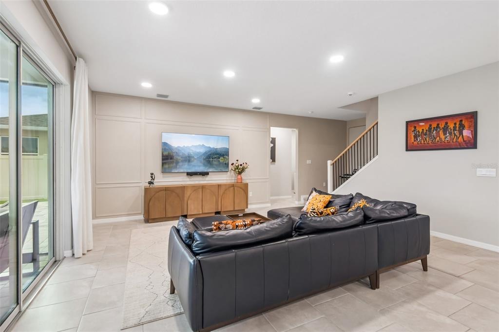 A living room features a dark leather sectional, a wall-mounted television, and beige wainscoting — 6076 WANDERING WILLOW DRIVE, WESLEY CHAPEL, FL