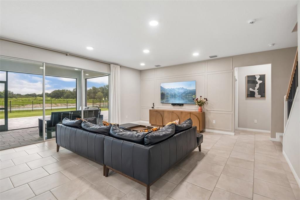 A living room features a dark leather sectional, a wall-mounted television, and large sliding glass doors — 6076 WANDERING WILLOW DRIVE, WESLEY CHAPEL, FL