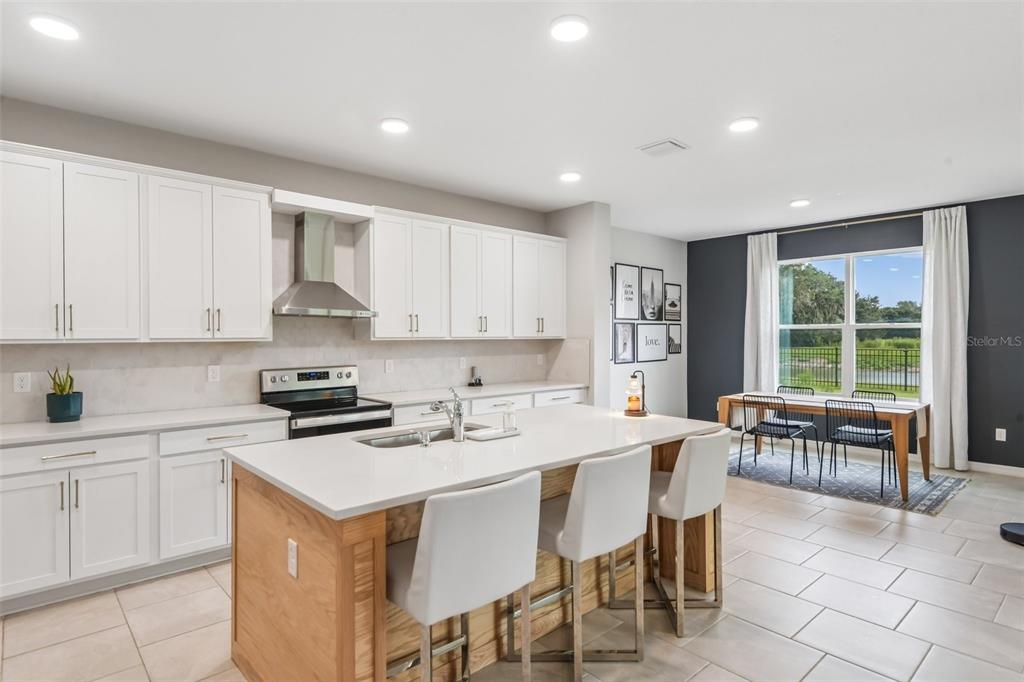 A kitchen with white cabinets, a wood-accented island, and an adjacent dining area with windows — 6076 WANDERING WILLOW DRIVE, WESLEY CHAPEL, FL
