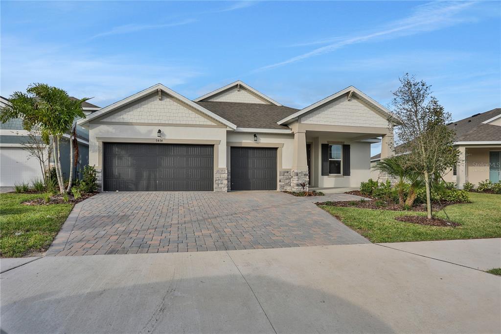 A single-story house features a three-car garage, a paver driveway, and a covered front porch — 7413 SEA MANATEE STREET, PARRISH, FL
