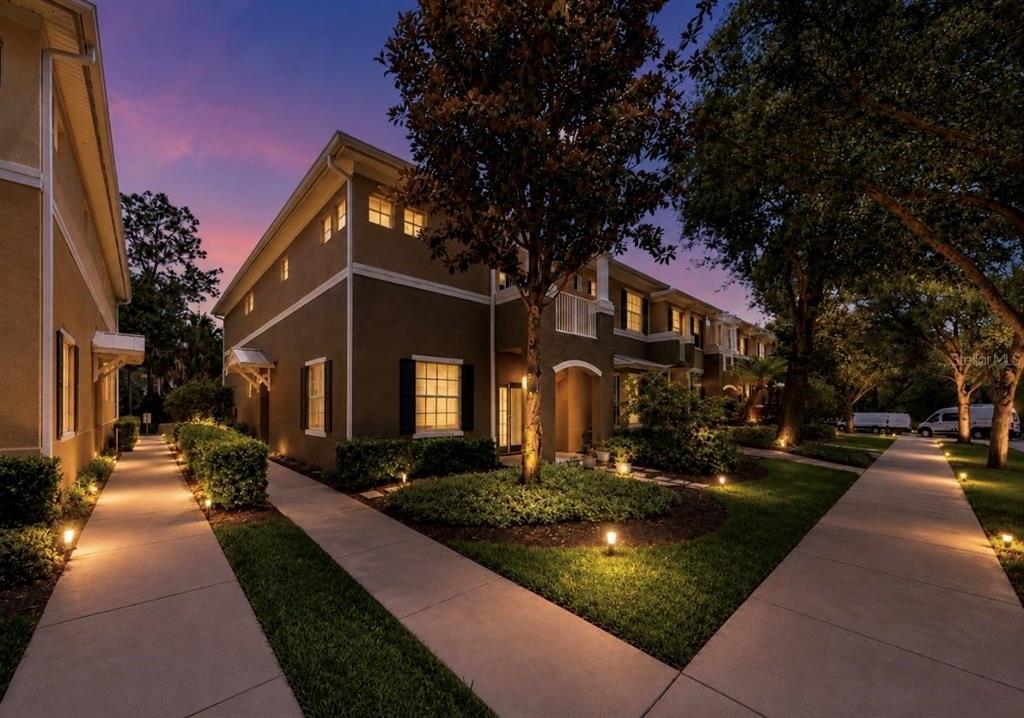 A two-story townhouse exterior at dusk with illuminated walkways and landscaping — 7539 TAMARIND AVENUE, TAMPA, FL