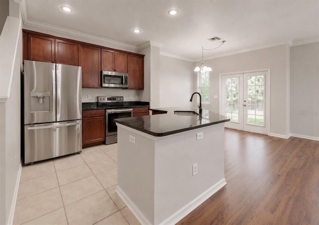 A kitchen with dark wood cabinets, stainless steel appliances, a granite island, and tile flooring — 7539 TAMARIND AVENUE, TAMPA, FL