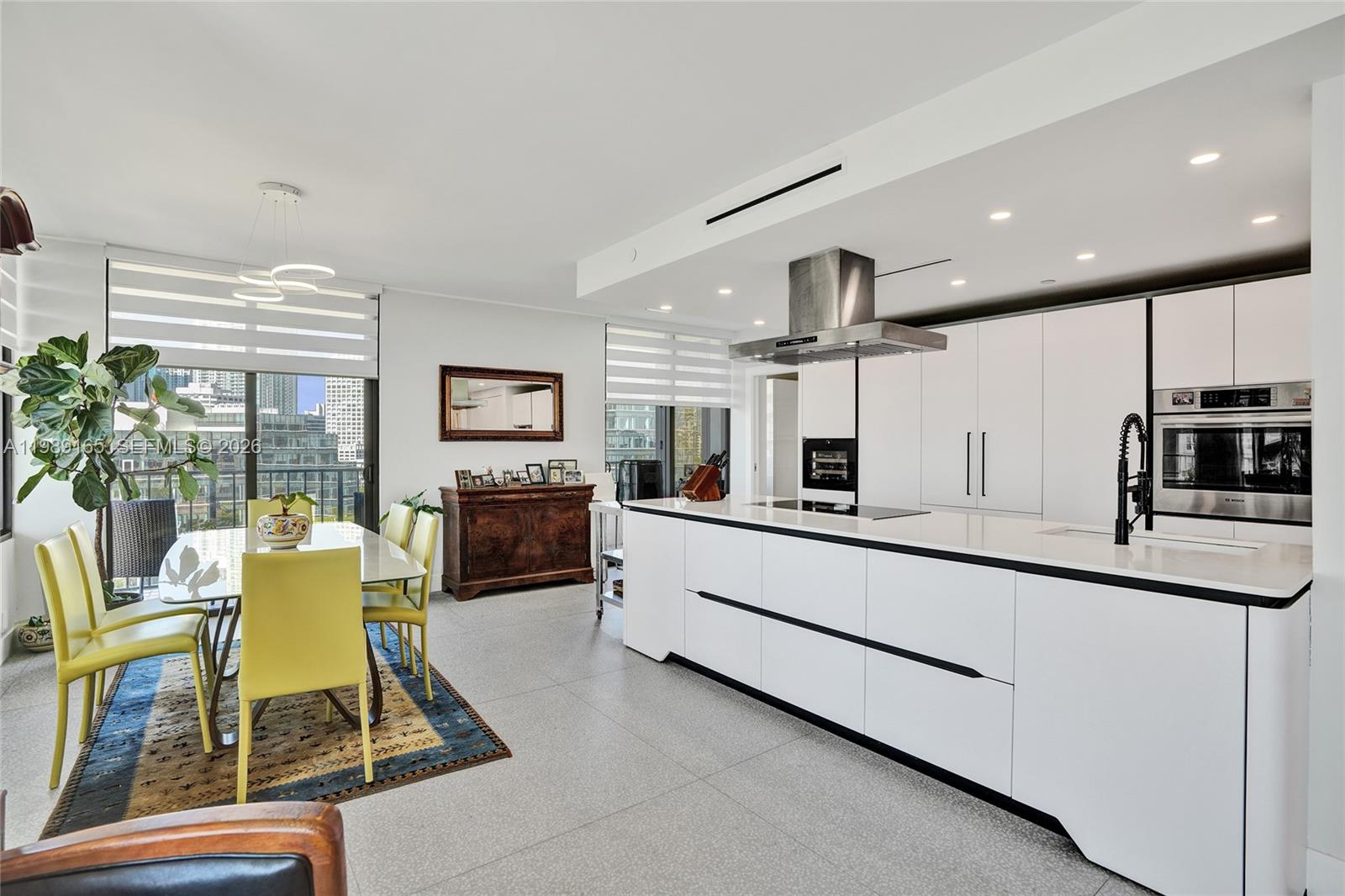 A modern kitchen and dining area feature white cabinetry, a large island, and city views — 520 Brickell Key Dr # A1015, Miami FL 33131, MIAMI, FL