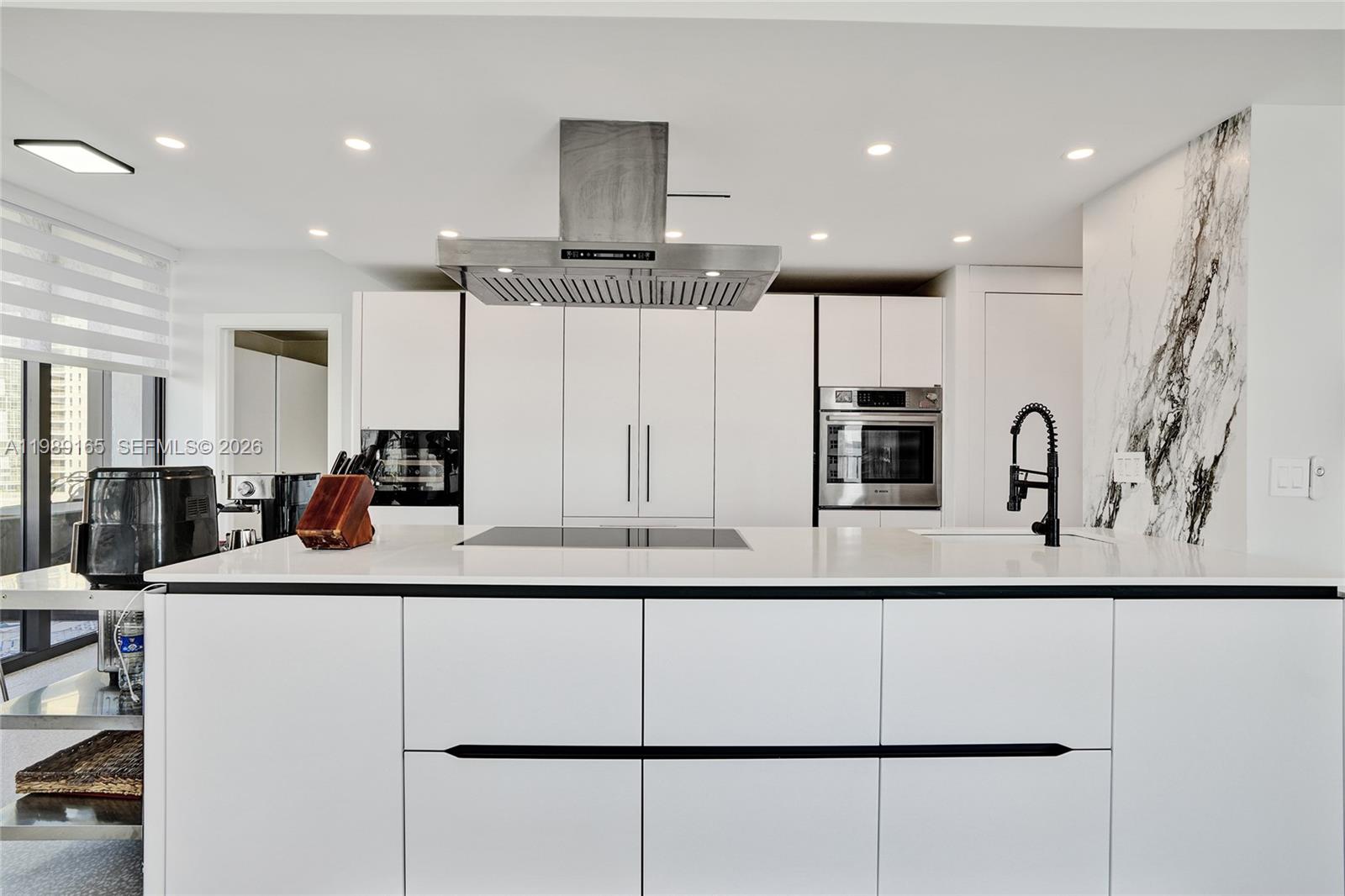 A modern kitchen features white cabinetry, a central island with a cooktop, and marble backsplash — 520 Brickell Key Dr # A1015, Miami FL 33131, MIAMI, FL