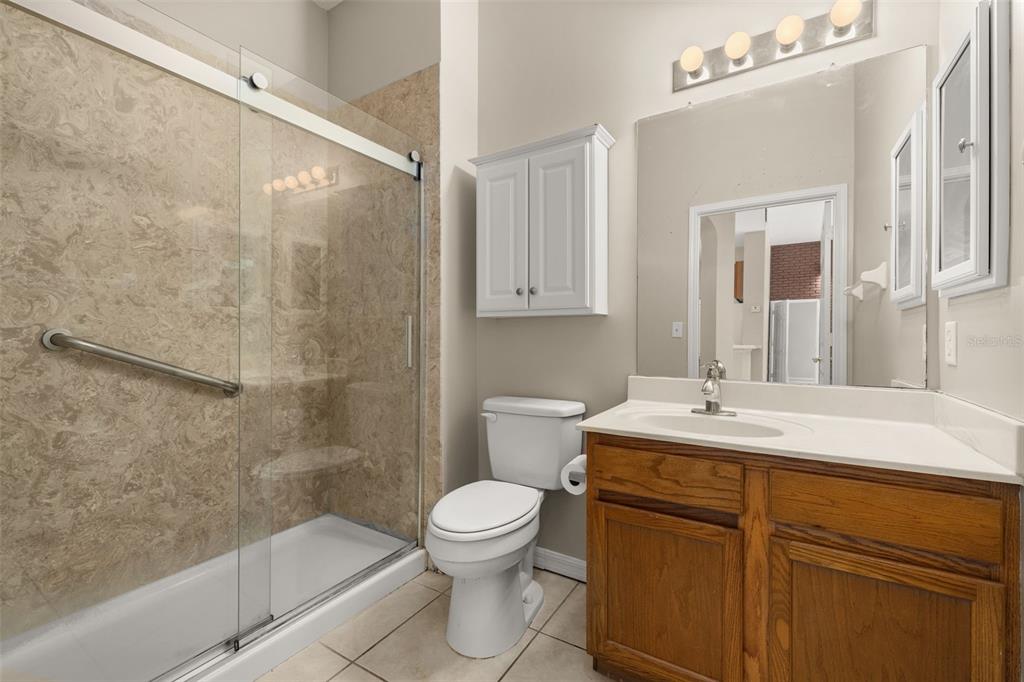 A bathroom features a glass-enclosed walk-in shower, a white toilet, and a wooden vanity — 949 WESTPARK DRIVE UNIT 106, KISSIMMEE, FL