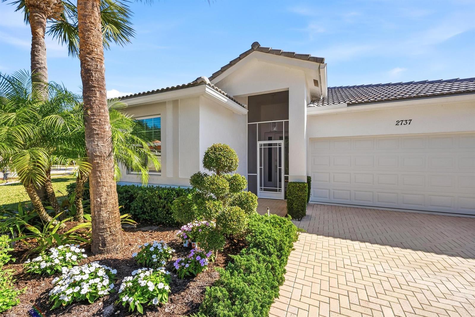 A white stucco house features a tiled roof, a paved driveway, and landscaped front gardens — 2737 Clipper Circle, West Palm Beach FL 33411, WEST PALM BEACH, FL