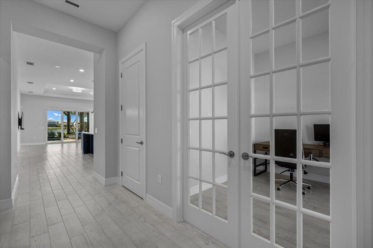 A hallway with light wood-look tile flooring leads to a room with French doors — 10366 Northbrook Circle, Palm Beach Gardens FL 33412, PALM BEACH GARDENS, FL