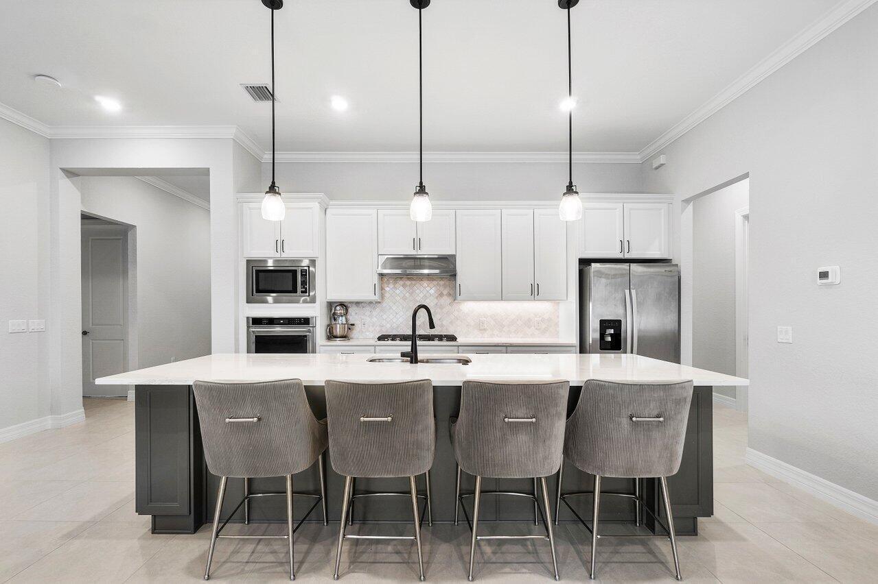 A modern kitchen features white cabinets, a dark gray island with four chairs, and stainless appliances — 9578 Mosler Trail, Lake Worth FL 33467, LAKE WORTH, FL