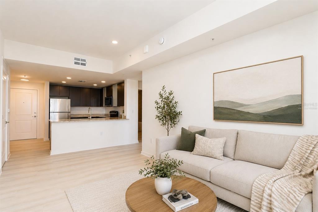 A living room with a beige sofa and a kitchen with stainless steel appliances — 5579 MILLENIA PARK BOULEVARD UNIT 401, ORLANDO, FL