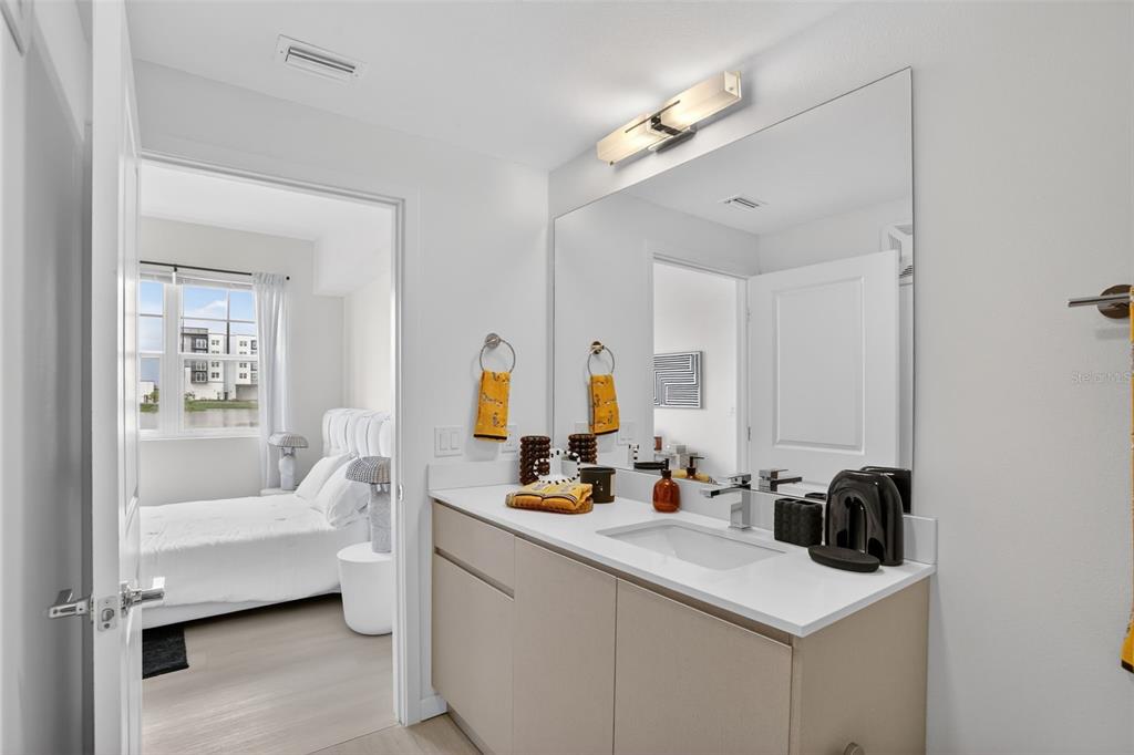A modern bathroom features a light-colored vanity, a large mirror, and a view into a bedroom — 5579 MILLENIA PARK BOULEVARD UNIT 401, ORLANDO, FL