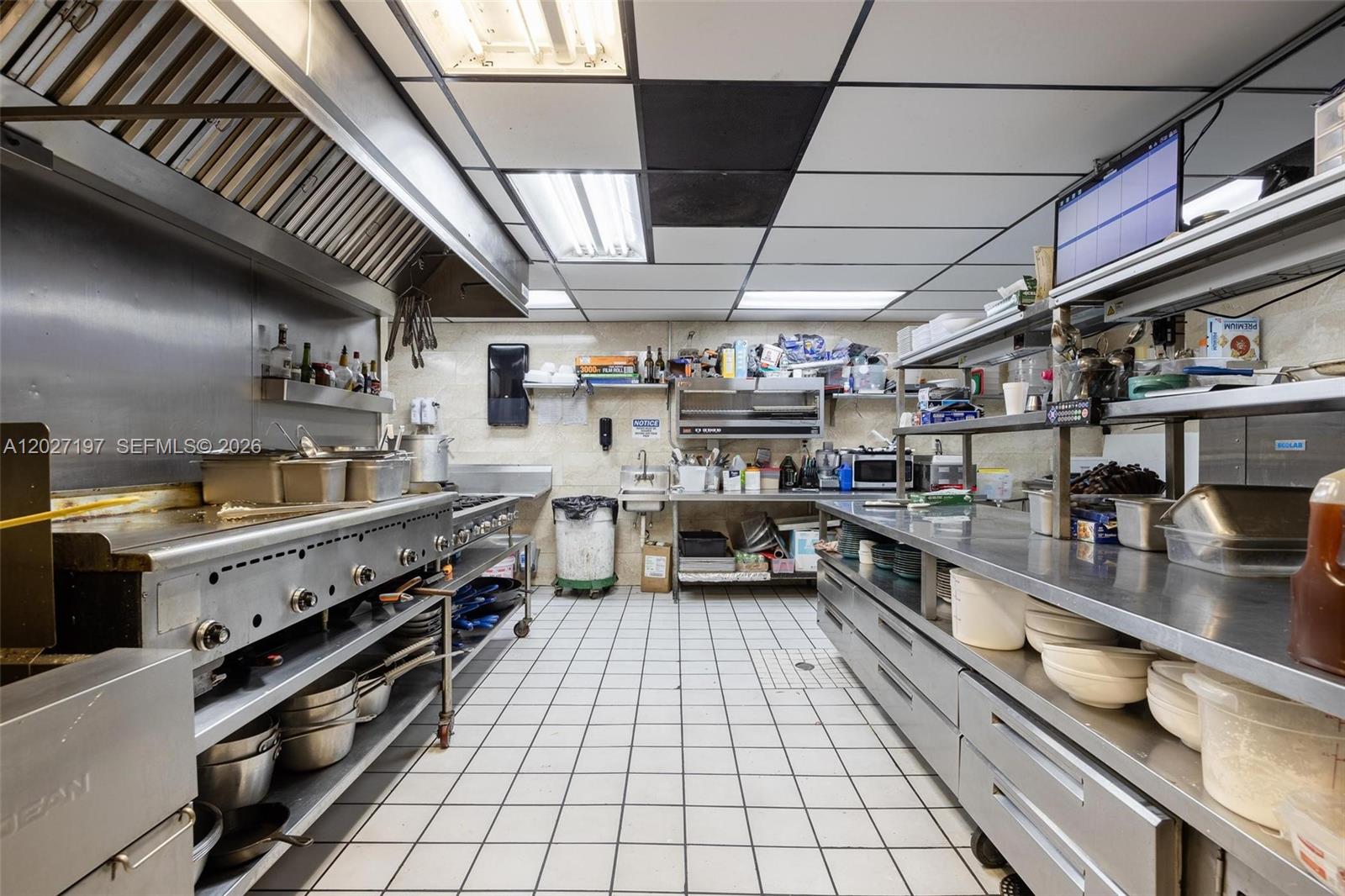 A commercial kitchen features stainless steel appliances, tiled flooring, and metal shelving units — 93 S Hall ST, La Belle FL 33935, LA BELLE, FL