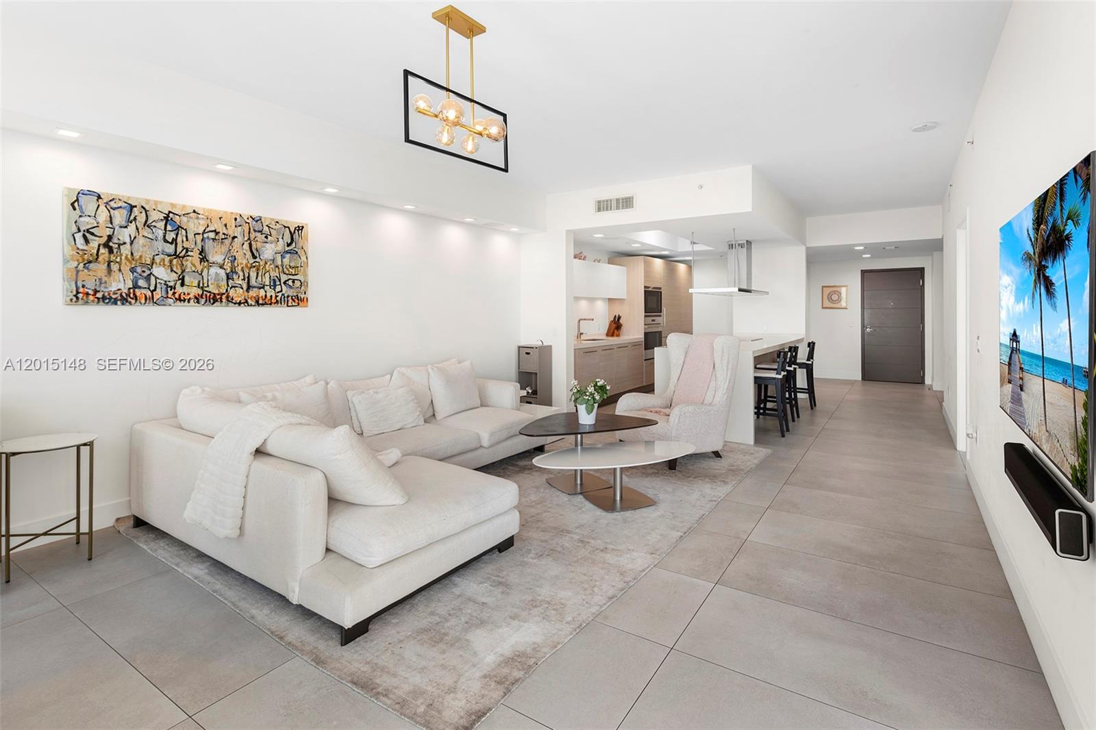 A modern living room features a white sectional sofa, a kitchen island, and tiled flooring — 17111 Biscayne Blvd # 606, North Miami Beach FL 33160, NORTH MIAMI BEACH, FL