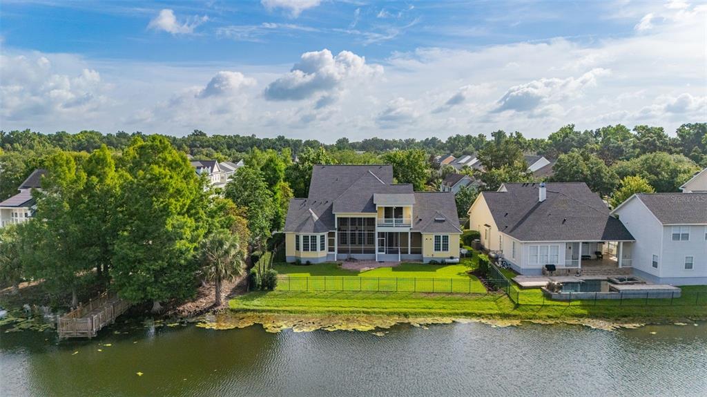 An aerial view shows a yellow two-story house with a screened porch overlooking a lake — 1247 AQUILA LOOP, CELEBRATION, FL