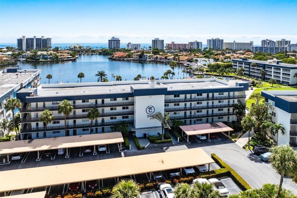 An aerial view shows a multi-story apartment building with covered parking and a nearby waterway — 3411 Spanish Trail # 418, Delray Beach FL 33483, DELRAY BEACH, FL