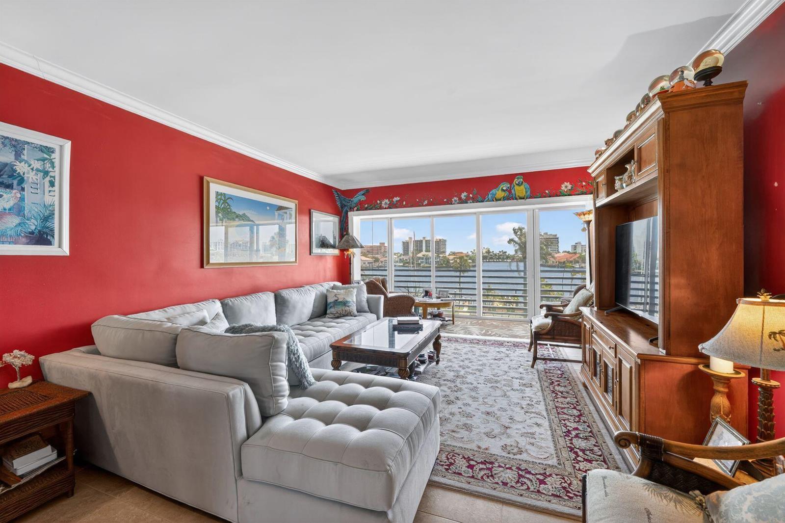 A living room with red walls, a grey sectional sofa, and a large window overlooking water — 3411 Spanish Trail # 418, Delray Beach FL 33483, DELRAY BEACH, FL