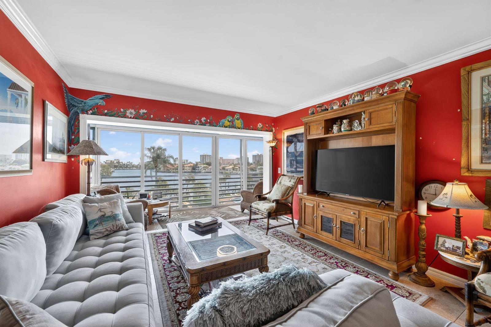 A living room with red walls, a large entertainment center, and floor-to-ceiling windows overlooking water — 3411 Spanish Trail # 418, Delray Beach FL 33483, DELRAY BEACH, FL