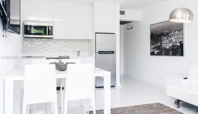 A modern kitchen features white cabinets, stainless steel appliances, and a dining table with chairs — 801 15th St # 208, Miami Beach FL 33139, MIAMI BEACH, FL