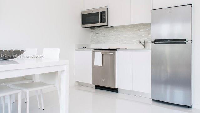 A modern kitchen features white cabinetry, stainless steel appliances, and a white dining table — 801 15th St # 208, Miami Beach FL 33139, MIAMI BEACH, FL
