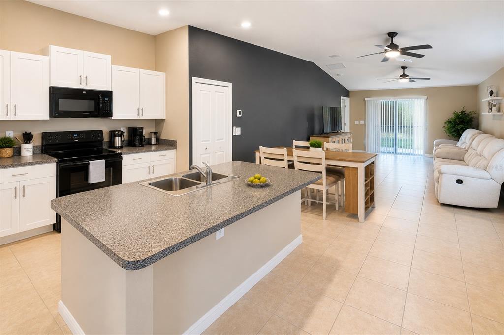 An open-concept kitchen with a granite island, white cabinets, and an adjacent dining and living area — 15446 BROAD BRUSH DRIVE, RUSKIN, FL