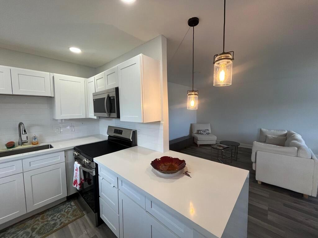 A white kitchen with a peninsula and pendant lights overlooks a living room area — 716 Monaco Court # 716, Delray Beach FL 33446, DELRAY BEACH, FL