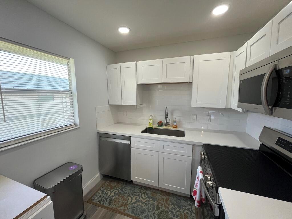 A kitchen features white cabinets, stainless steel appliances, a subway tile backsplash, and a window — 716 Monaco Court # 716, Delray Beach FL 33446, DELRAY BEACH, FL