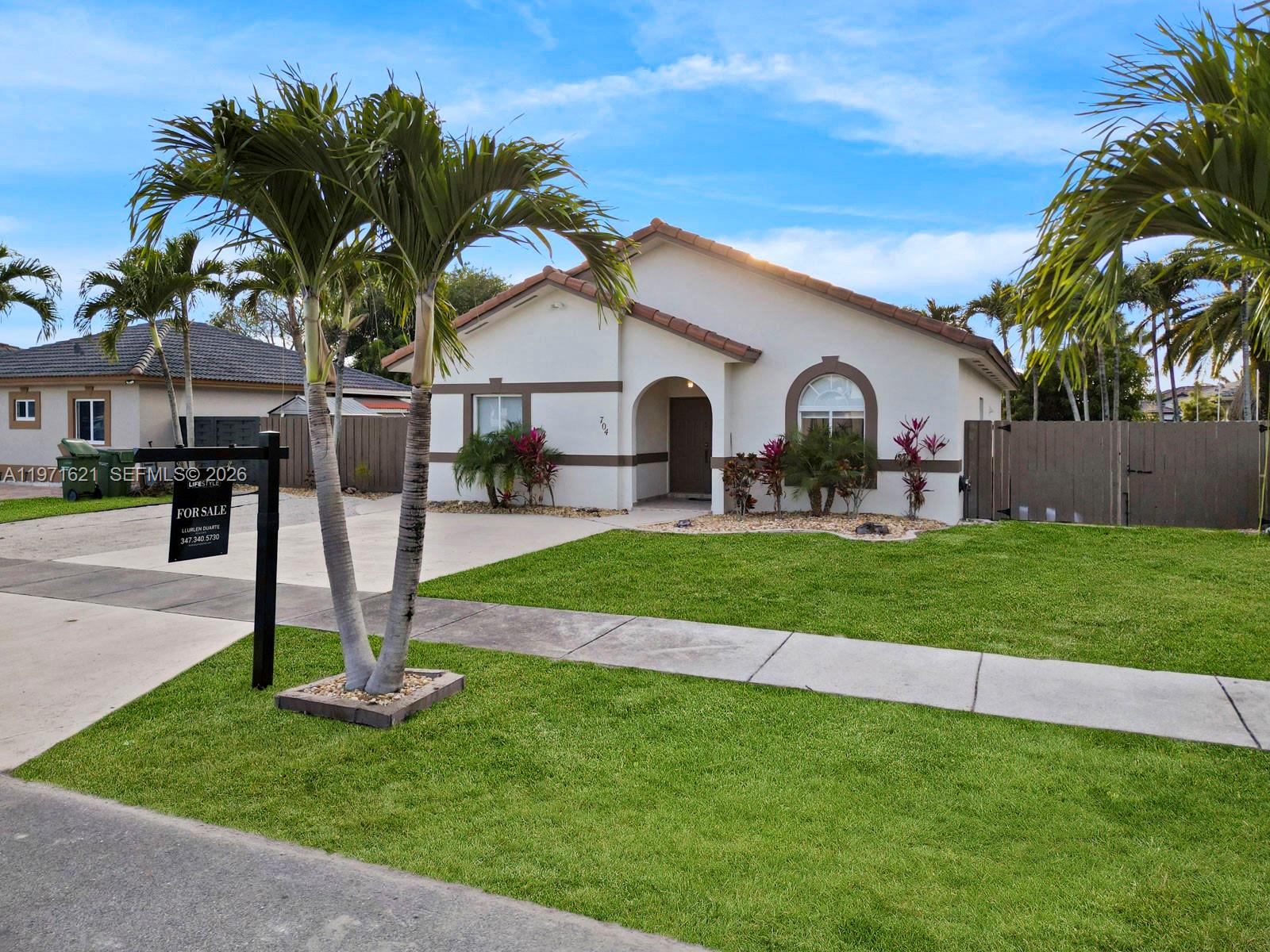 A single-story house with a tiled roof, palm trees, and a for-sale sign in front — 704 SE 14th Pl, Homestead FL 33033, HOMESTEAD, FL