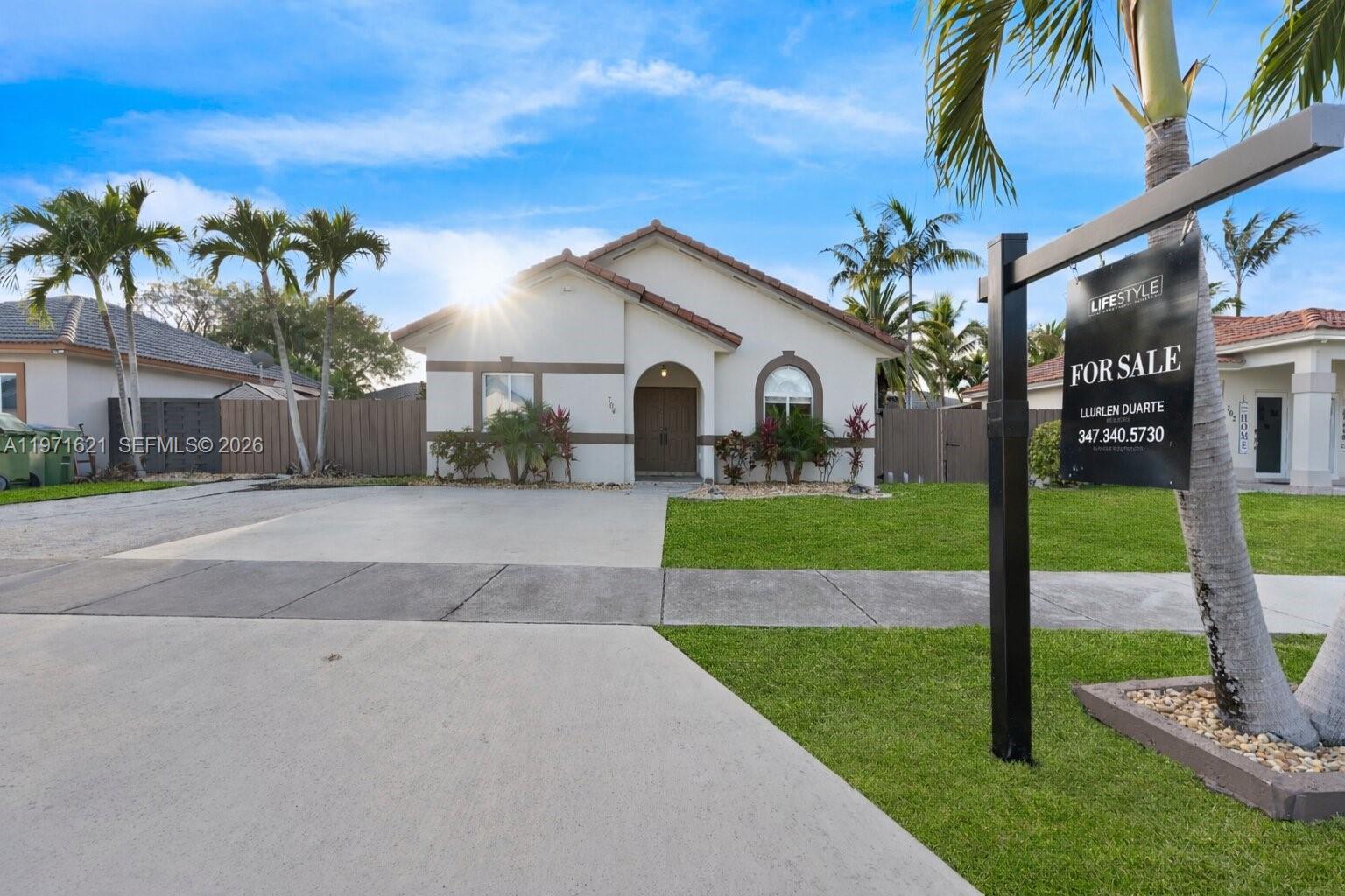 A single-story house with a concrete driveway and a for sale sign in the yard — 704 SE 14th Pl, Homestead FL 33033, HOMESTEAD, FL